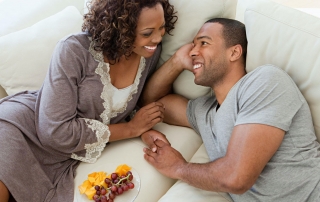 African American couple smiling, looking at each other, lying on couch